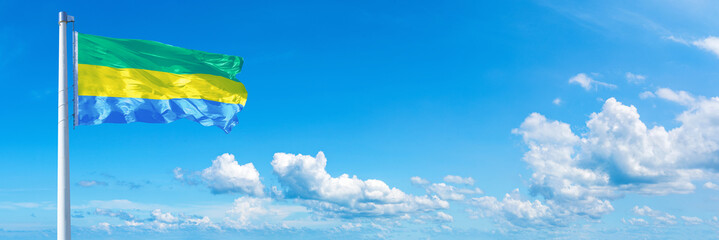 Obraz na płótnie Canvas Gabon flag waving on a blue sky in beautiful clouds - Horizontal banner