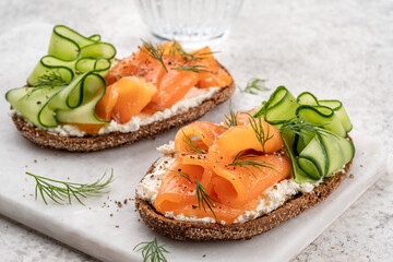 Rye bread open sandwiches with salted salmon and cucumber on a white stone table. Healthy food.