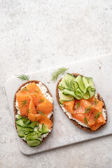 Rye bread open sandwiches with salted salmon and cucumber on a white stone table. Healthy food.