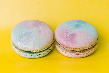 Tasty colorful macaroon. Two blue and pink macaroons on a yellow background. Most delicate cake is a cookie made of two smooth halves, fastened with fillings. French pastry made from egg whites.