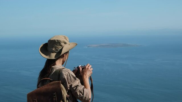 Robben Island, Cape Town, South Africa. a girl tourist in a hat stands on a table mountain in cape town and takes a photo of Robben Island, ocean South Africa Nelson Mandela prison.