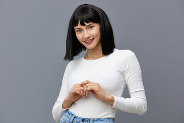 Obraz premium a calm woman stands against a dark background in a tight white T-shirt, looking down confusedly holding her hands in front of her
