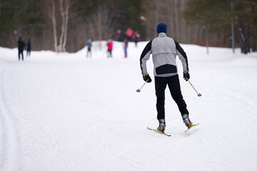 Winter. Weekend. A man is happy to slide on a ski track in the forest. A group of people in the distance. Selective focus.