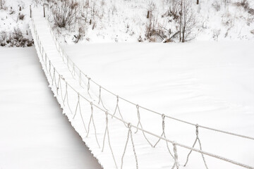 Winter. Pedestrian hanging rope bridge over a frozen pond. Copy space.