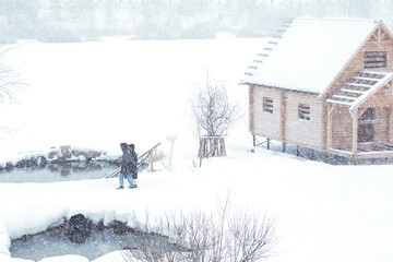 Construction of a small wooden house on a pile foundation by the river. A hole has been cut and equipped with a ladder at the house. Winter. Blizzard.