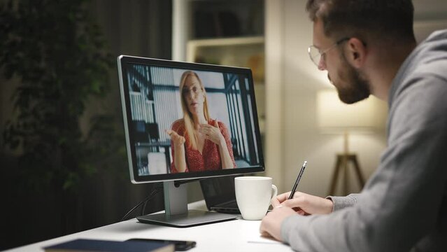 Young concentrated caucasian male having videochat with felmale tacher and writing down information, online education.