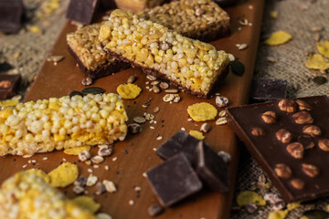 Bar with granola, dried fruits and nuts on a wooden board with dried fruits, nuts, chocolate and cereals