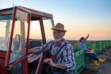 Senior farmer and young woman beside tractor and crates after apple harvest