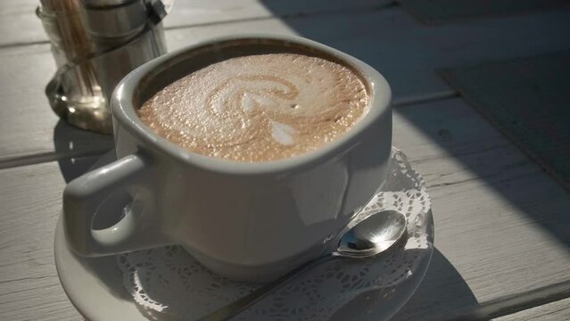 Cup of cappuccino on the table in summer cafe with sunlight and hard shadows. 4k video