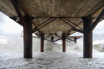 Large waves breaking on the poles of the pier, view from under the pier