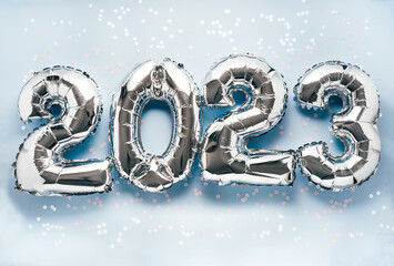 Shiny silber air balloon numbers on light blue background with confetti and decorations. 2023 New...