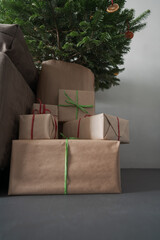 presents in paper wrap with ribbons under christmas tree indoor near couch with natural light
