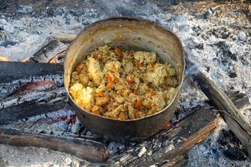 Camping black kettle with pilaf on the coals of a fire. Smoke from burning coals