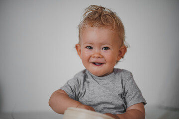 cute happy one year old blond baby boy in casual outfit at home on a cozy sofa smiling or looking...