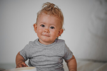 Naklejka premium cute happy one year old blond baby boy in casual outfit at home on a cozy sofa smiling or looking into the Camera while open can or box