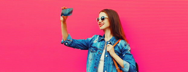 Portrait of happy smiling young woman taking selfie with smartphone wearing backpack on pink...