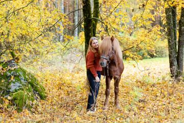 Fototapeta premium Young woman under yellow maple tree with Icelandic horse