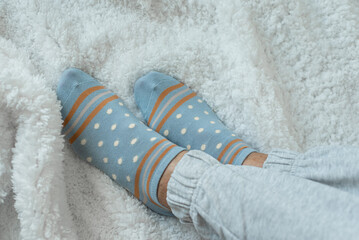 Women's legs in socks and warm gray pants on a white fluffy plaid, at home in a cozy autumn season. Rest at home after a hard day's work.