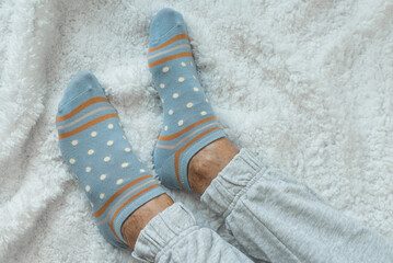 Women's legs in socks on a white fluffy plaid, at home in a cozy autumn season. Rest at home after a hard day's work. Varicose veins on legs. Swollen legs, problems with the bone in the legs.