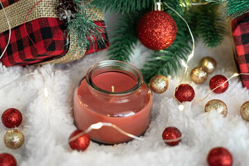 Red candle,gifts in a checkered cloth wrapper, yellow lights on a garland, a sprig of a Christmas tree on a white soft background.  Postcard for the New Year and Christmas.