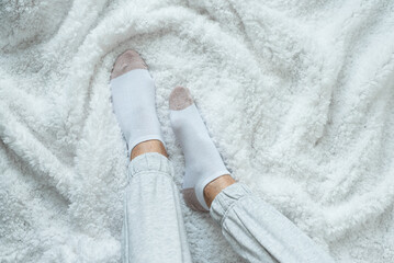 Women's legs in socks and warm gray pants on a white fluffy plaid, at home in a cozy autumn season.
