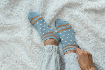 Women's hands put on socks higher while sitting on a white fluffy plaid. Cozy cold autumn time to stay at home. Top view 