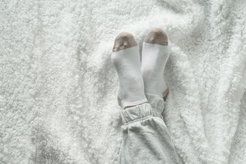 Women's legs in socks on a white fluffy plaid, at home in a cozy autumn season. Top view