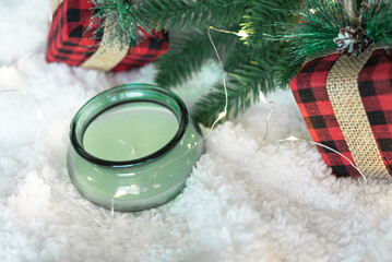 Green candle,gifts in a checkered cloth wrapper, yellow lights on a garland, a sprig of a Christmas tree on a white soft background. Focus on the gift. Postcard for the New Year and Christmas.