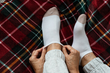 Women's hands put socks on legs sitting on a red checkered plaid. Rest at home after a hard day's work.