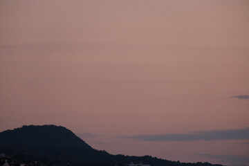早朝の甲山。太陽が東の空に昇り稜線も徐々に明るくなる。神戸市街地より六甲山系と甲山を望遠レンズで切り取る - obrazy, fototapety, plakaty