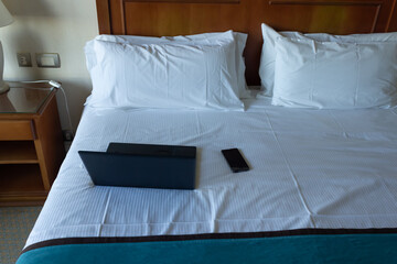 Fototapeta na wymiar Laptop and cell phone on a bed with pillows and white sheets.