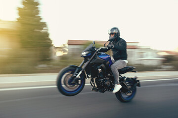Side view of a motorcycle rider riding race motorcycle on a wheelie the highway with motion blur. - obrazy, fototapety, plakaty