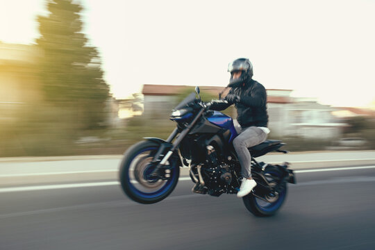 Side view of a motorcycle rider riding race motorcycle on a wheelie the highway with motion blur.