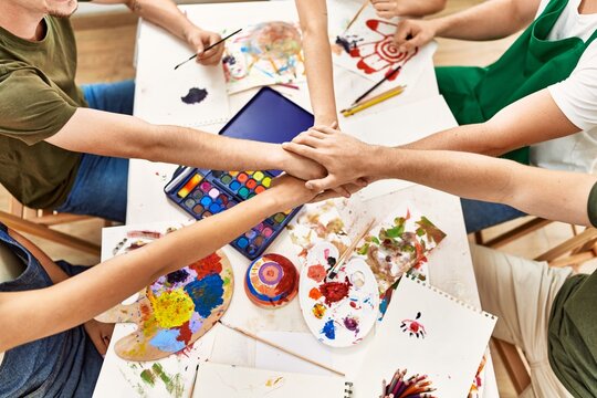 Group of people sitting on the table with united hands at art studio.