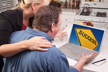 Fototapeta na wymiar Couple In Kitchen Looking at a Success Road Sign on Their Laptop 