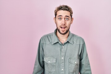 Hispanic man with beard standing over pink background afraid and shocked with surprise expression, fear and excited face.
