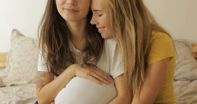 pregnant multiethnic lesbian couple lies in bed are very happy that they will have a baby. at home