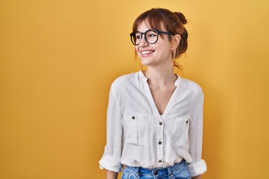 Young beautiful woman wearing casual shirt over yellow background looking away to side with smile on face, natural expression. laughing confident.