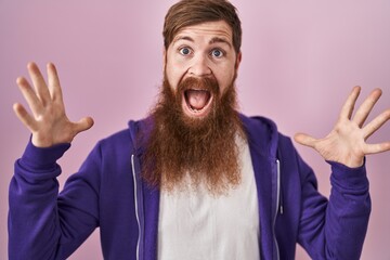 Caucasian man with long beard standing over pink background celebrating crazy and amazed for success with arms raised and open eyes screaming excited. winner concept