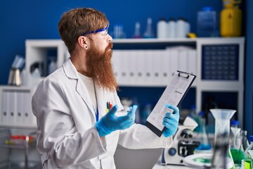 Young redhead man scientist reading report holding sample at laboratory