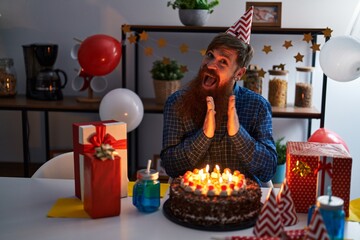 Young redhead man celebrating birthday sitting on table at home