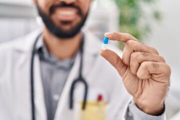 Young hispanic man doctor holding pill at clinic