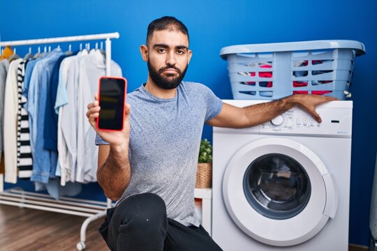 Middle east man with beard showing smartphone screen and washing machine depressed and worry for distress, crying angry and afraid. sad expression.