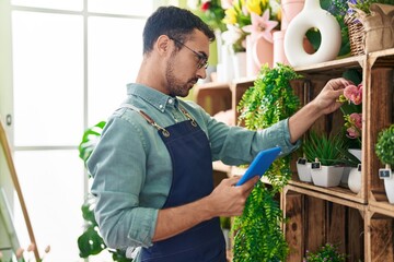 Young hispanic man florist using touchpad at flower shop