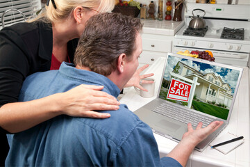 Couple In Kitchen Looking at a For Sale Real Estate Sign on Their Laptop 