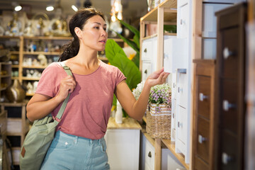 Adult Asian woman choosing bedside table in furniture store.