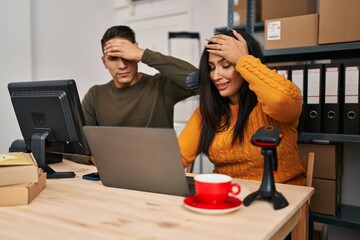 Young woman and man working at small business ecommerce stressed and frustrated with hand on head, surprised and angry face