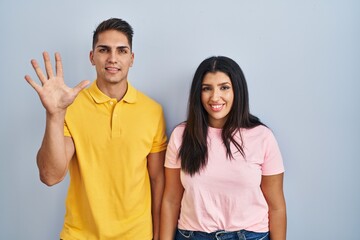 Young couple standing over isolated background showing and pointing up with fingers number five while smiling confident and happy.