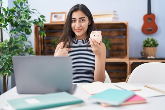 Young teenager girl studying using computer laptop pointing finger to one self smiling happy and proud
