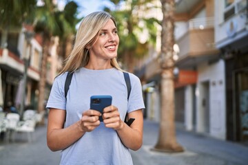 Young blonde woman smiling confident using smartphone at street